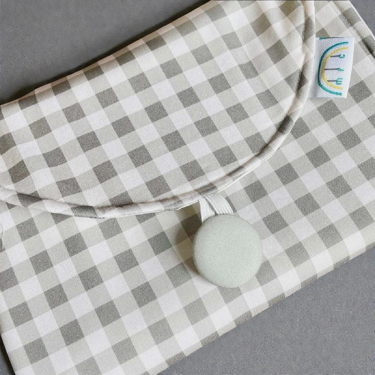 sage green and white gingham change mat with a button closure on a gray background