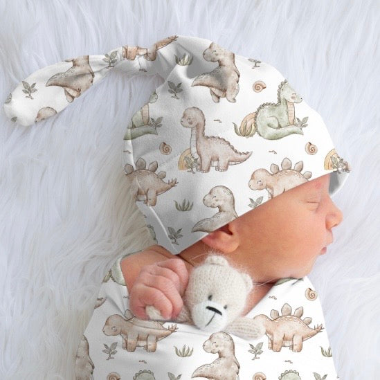 Baby wearing a dinosaur-patterned hat and onesie on a soft white background