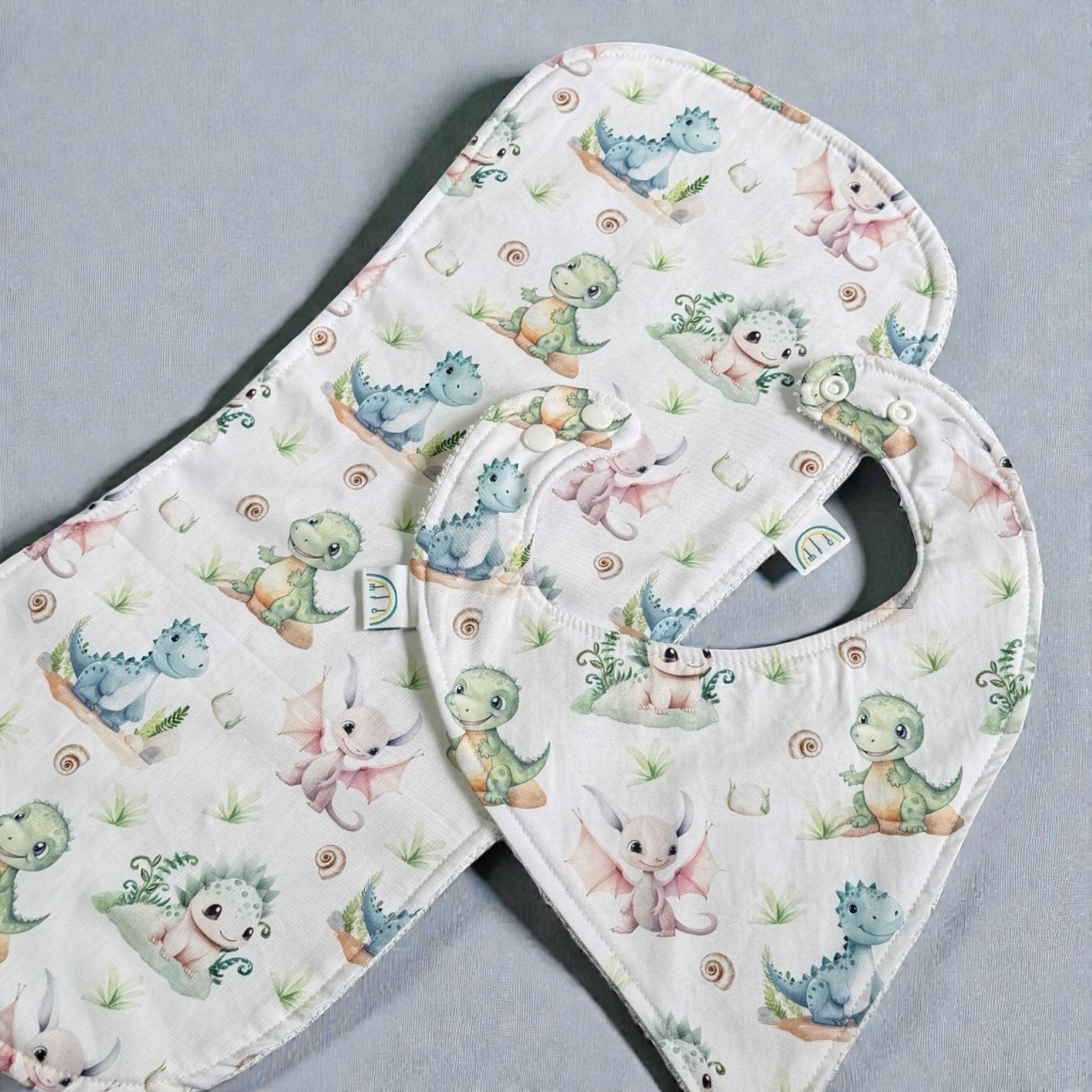 Baby bib and burp cloth set with dinosaur and animal pattern on a gray background
