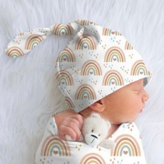 Newborn baby wearing a rainbow-patterned top knot beanie and swaddle on a white background