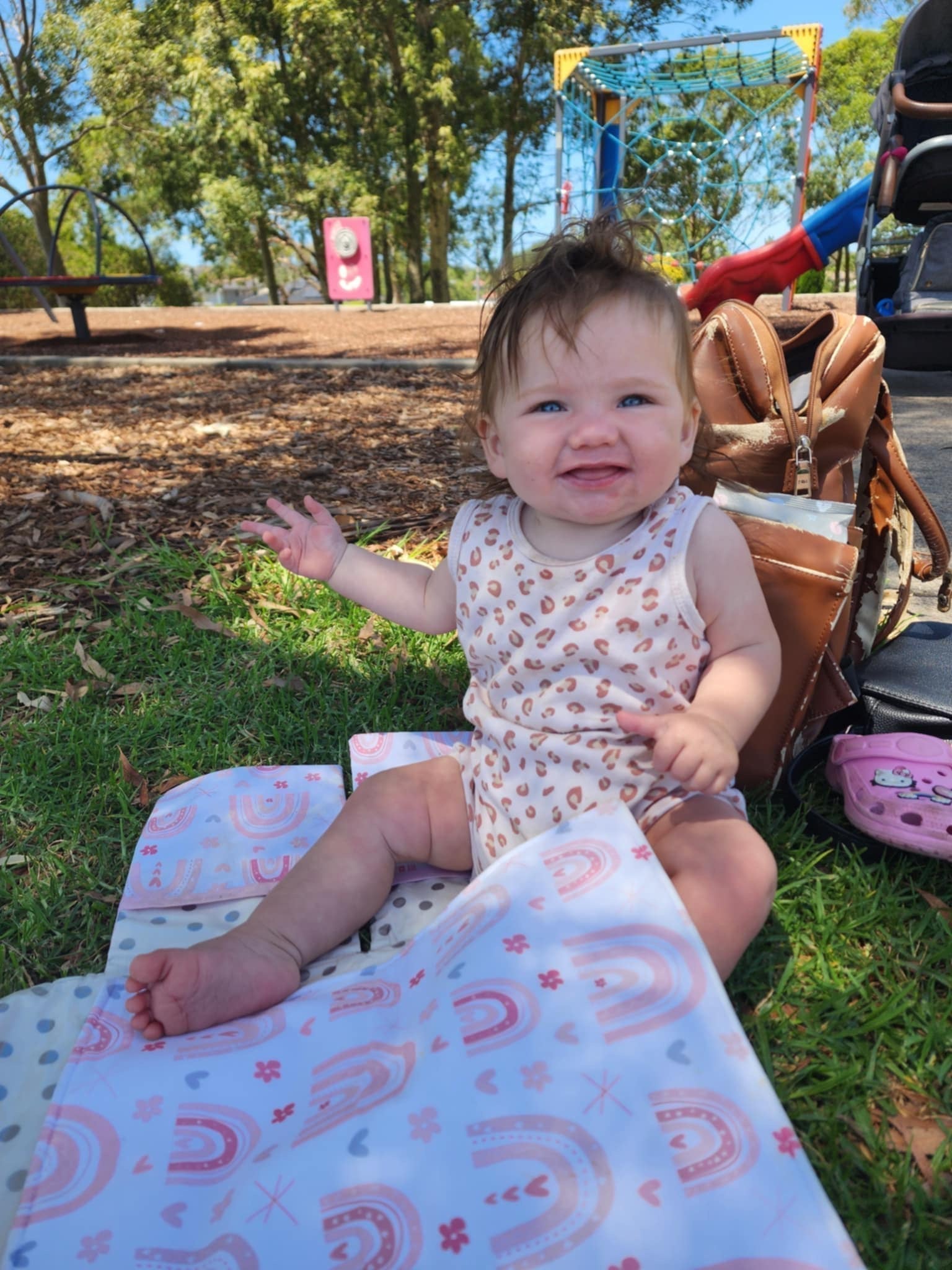 baby sitting on a change mat on the grass at a park