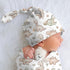 Baby wearing a dinosaur-patterned hat and onesie on a soft white background