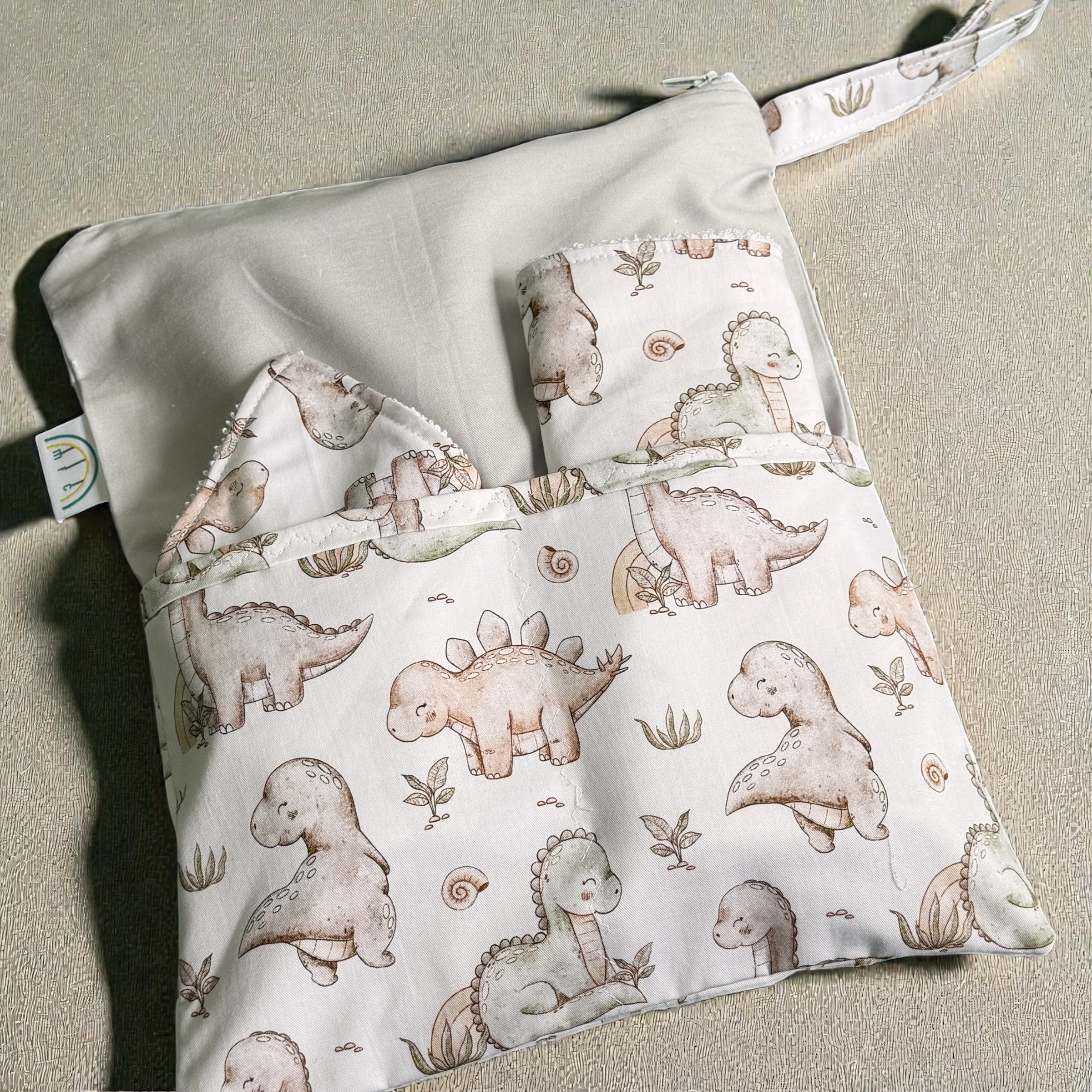 Baby change mat bib and burp cloth with dinosaur pattern on a beige surface
