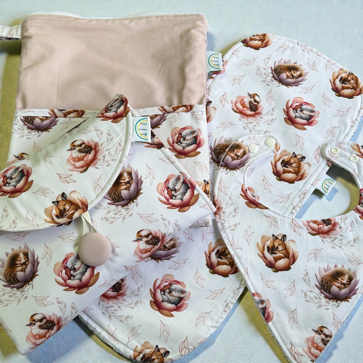 Floral Australian sleeping animals fabric with baby change mat baby bibs and a pink pouch on a light blue background