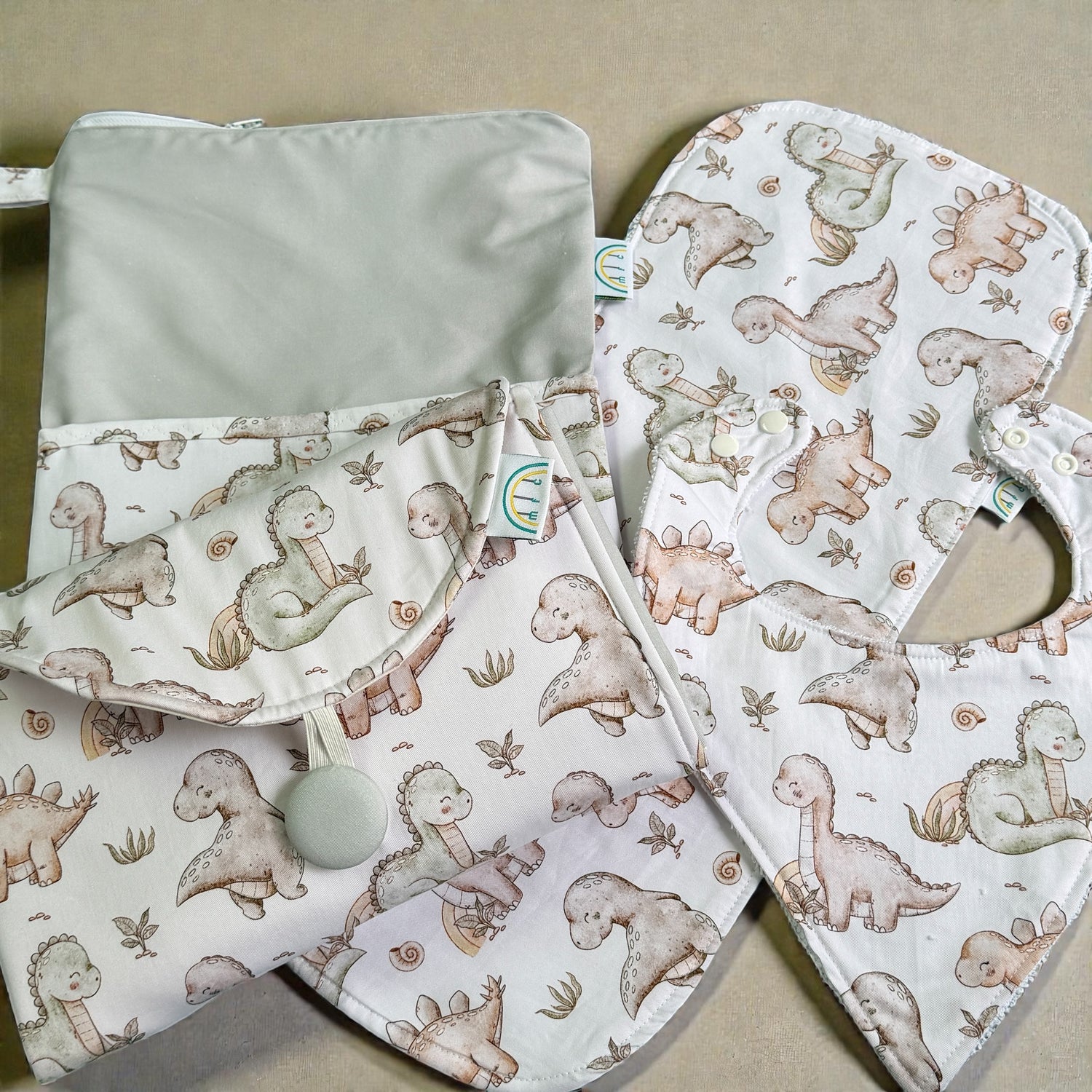 Baby bib and changing mat with dinosaur pattern on a white and sage  background