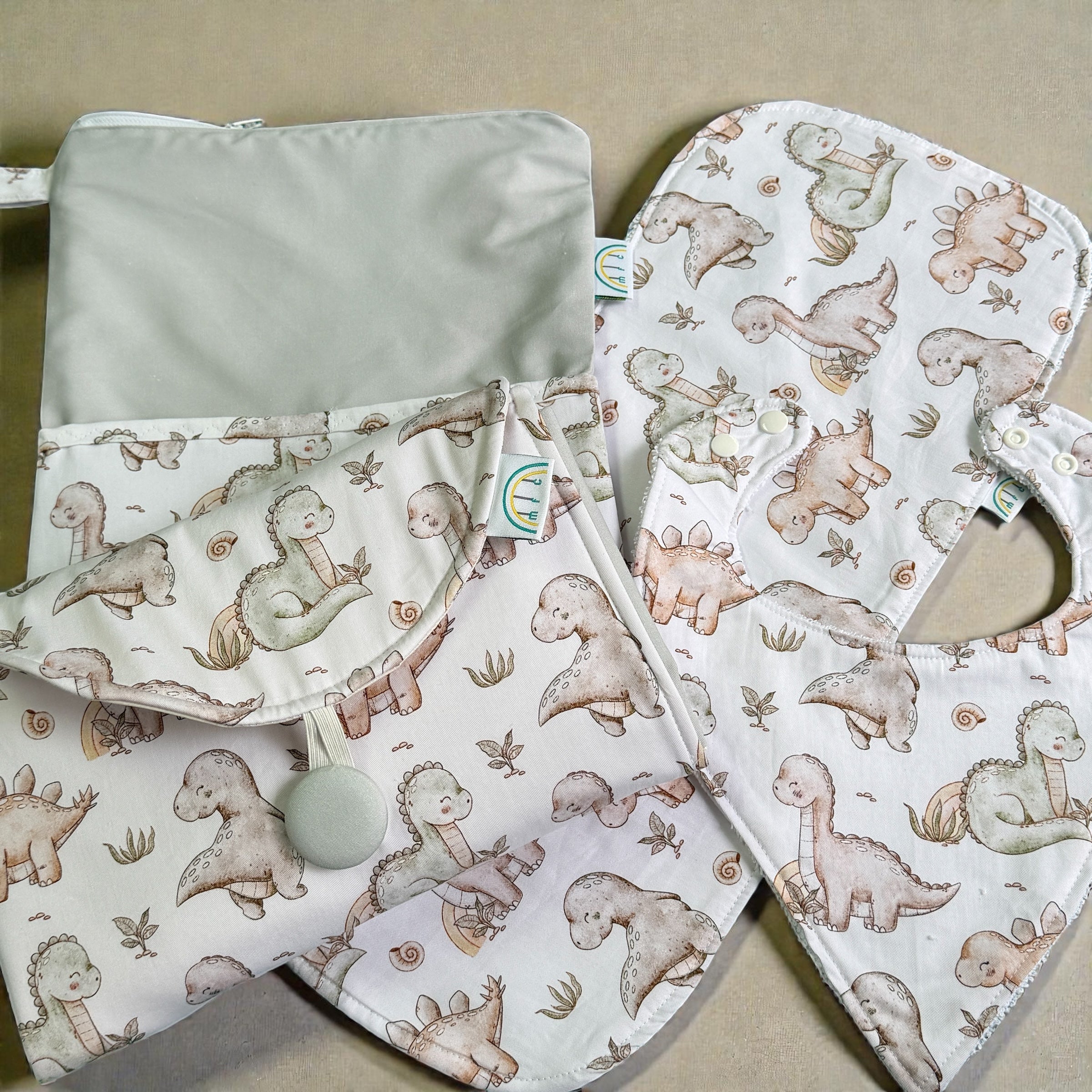 Baby bib and changing mat with dinosaur pattern on a white and sage  background
