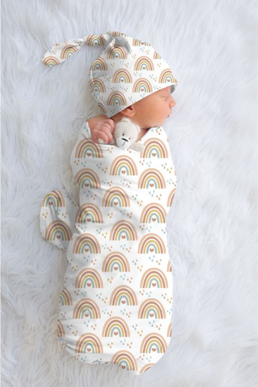 Newborn baby wrapped in a rainbow-patterned swaddle with matching hat on a light gray background