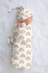 Newborn baby wrapped in a rainbow-patterned swaddle with matching hat on a light gray background