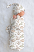 Newborn baby wrapped in a dinosaur-patterned swaddle blanket with matching hat on a soft white background