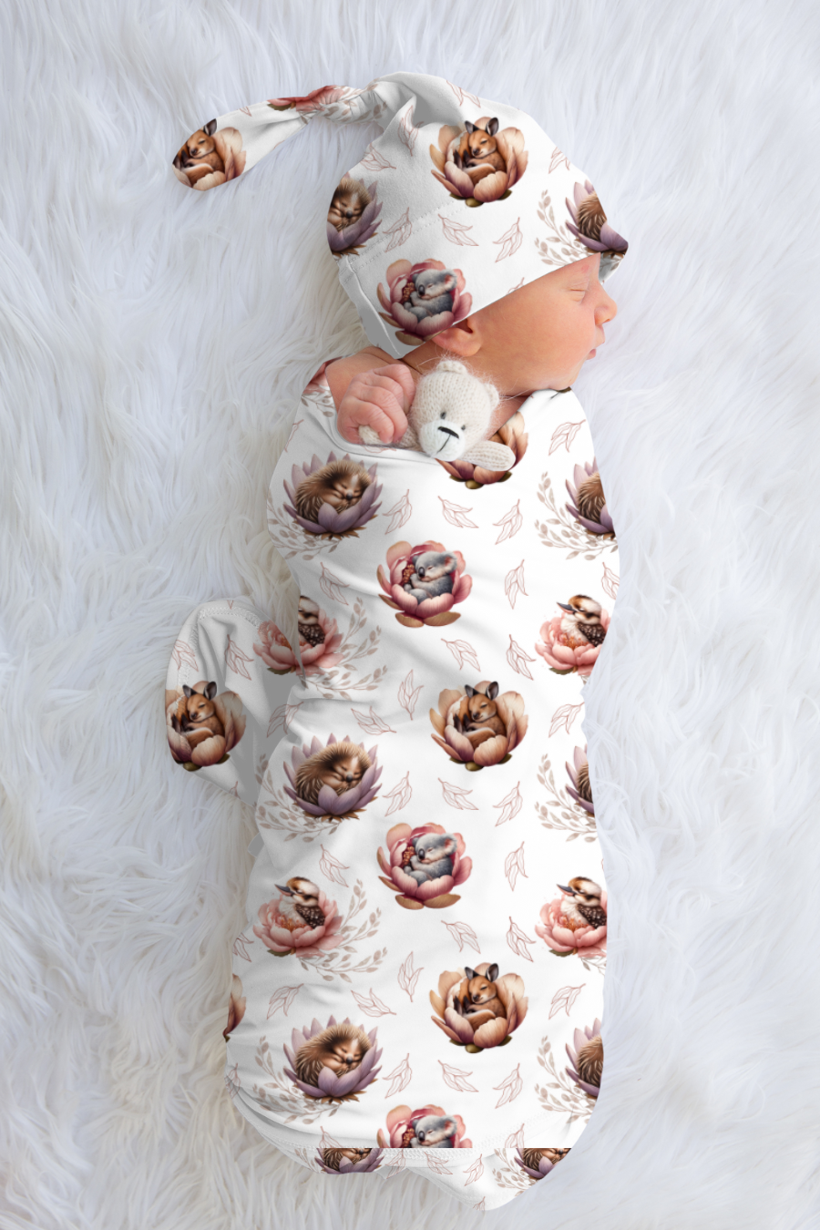 Baby wrapped in a floral baby animal patterned blanket on a white surface