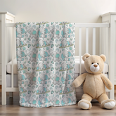 blanket with blue and grey elephants with hearts over the side of a cot with a small teddy 