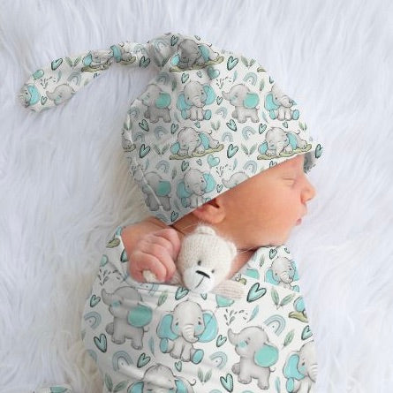 A newborn baby wrapped in a blue and grey elephant patterned swaddle, with a matching beanie on the head.