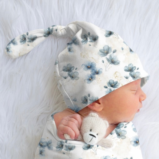 Baby wearing a floral hat and holding a teddy bear on a white background