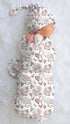 A baby swaddle wrap with a pink elephant and hearts pattern, displayed on a white fluffy surface.