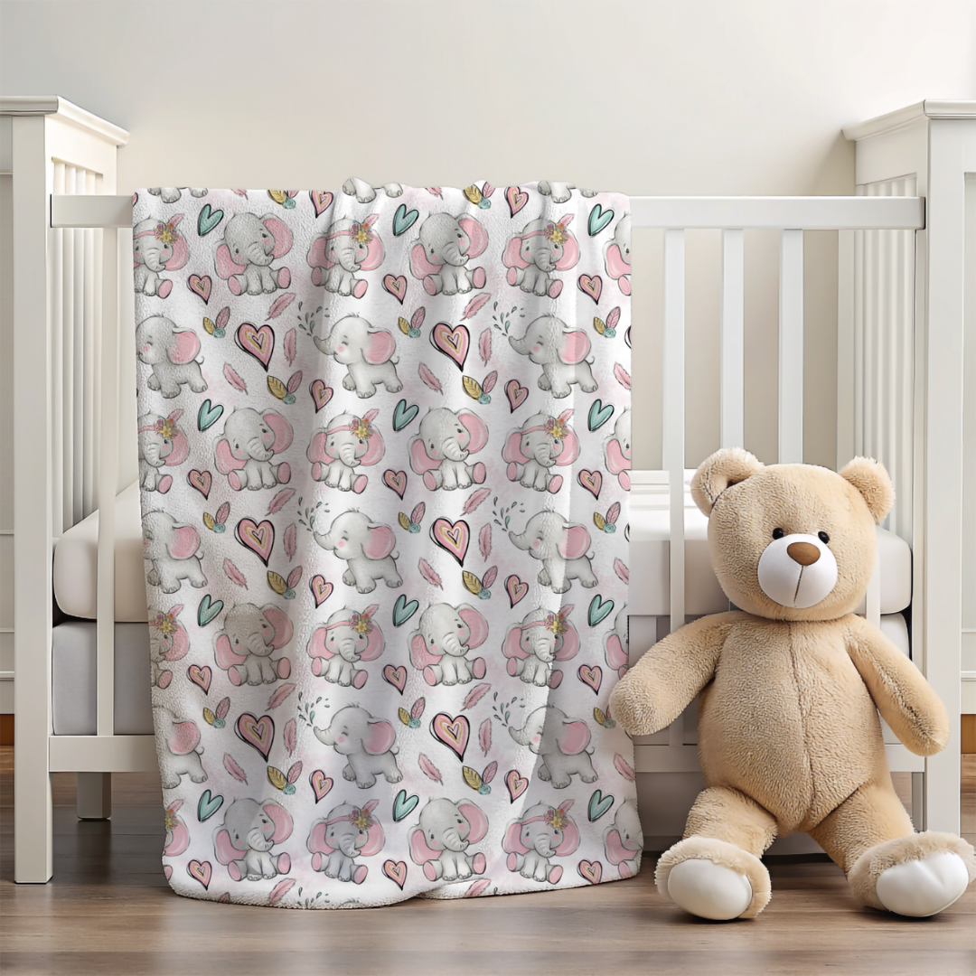 baby blanket with pink and grey elephants and hearts over a cot side with a small teddy 